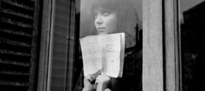 alphaville-1965-006-anna-karina-behind-glass-door-holding-book-00o-4cd-1000×444